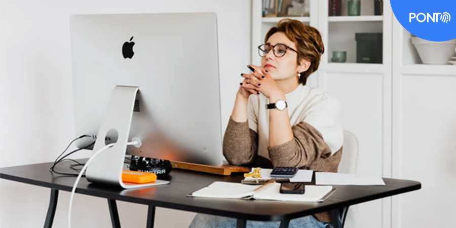 Imagem de uma mulher de meia idade, com cabelo curto, olhando a tela de um computador da marca Apple.